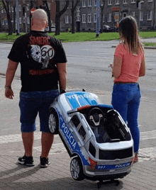 a man wearing a shirt that says śmierc is pushing a toy police car