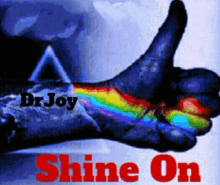 a hand with a rainbow painted on it giving a thumbs up with the words dr joy shine on below it