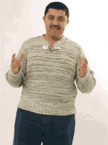 a man wearing a grey sweater and blue jeans is giving the peace sign