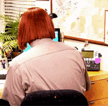 a woman with red hair is sitting at a desk with a phone and a map on the wall behind her