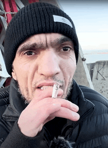 a man wearing a black beanie smoking a cigarette with the letter g on it