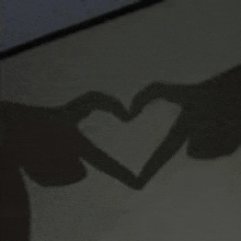 a couple of hands making a heart shape with their shadows .