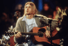 a man playing a guitar and singing into a microphone with a shirt that says nirvana on it