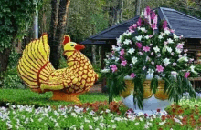 a yellow chicken made of flowers is sitting next to a vase of flowers in a garden .