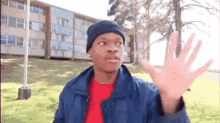 a man in a blue jacket and red shirt is standing in front of a building and waving his hand .