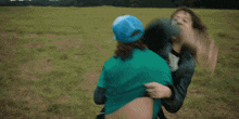 a woman in a blue hat is holding another woman in a field .