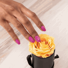 a woman 's hand with purple nails is reaching for a yellow rose