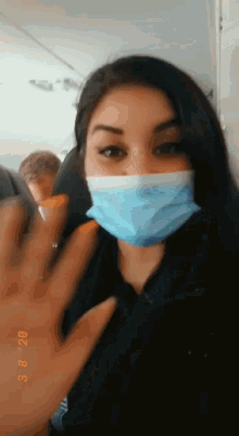 a woman wearing a mask on an airplane is waving at the camera .