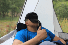 a man in a blue shirt is giving a thumbs up in front of a white tent