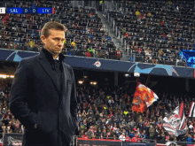 a man in a suit stands in front of a crowd at a soccer game with the scoreboard showing sal 0 liv