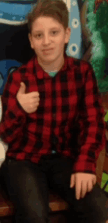 a young boy in a red and black plaid shirt gives a thumbs up