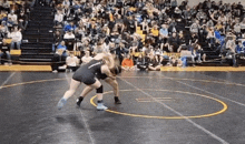 two wrestlers are wrestling on a wrestling mat in front of a crowd in a gym .