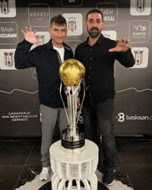 two men standing next to a trophy that says 3 baskisan.com