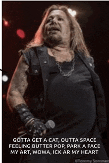 a man with long hair is singing into a microphone while wearing a black vest and gloves