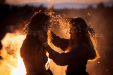 two women wearing wreaths of flowers on their heads in front of a fire .