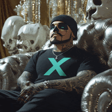 a man wearing a black shirt with a green x on it sits on a couch