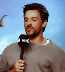 a man wearing a grey sweater is holding a bbc radio microphone