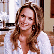 a woman wearing a white shirt and earrings smiles for the camera