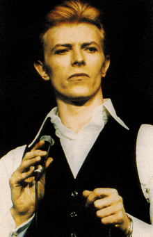 a man in a black vest and white shirt holds a microphone