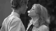 a man and a woman are blowing bubble gum and kissing .