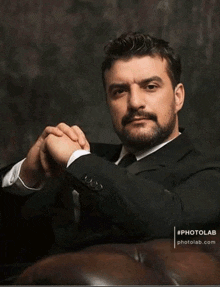 a man with a beard is sitting on a couch with his hands folded