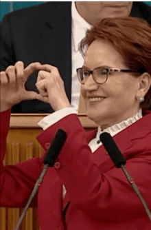 a woman wearing glasses and a red jacket is making a heart with her hands