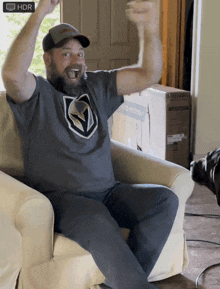 a man wearing a vegas golden knights shirt is sitting on a couch with his arms up in the air