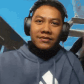 a man wearing headphones and a blue hoodie is standing in front of a blue background .