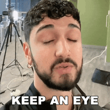 a man with a beard says " keep an eye " in front of a tripod