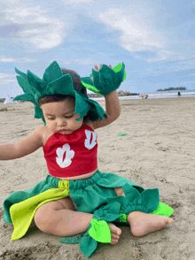 a little girl in a red top and green skirt is sitting on a beach