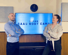 a man and woman stand in front of a screen that says saas boot camp