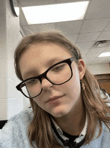 a girl wearing glasses and a blue sweater looks at the camera