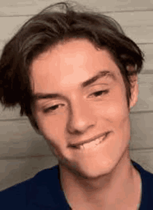 a close up of a young man making a funny face while wearing a blue shirt .