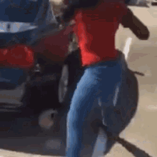 a woman in a red shirt and blue jeans is walking down a street next to a red car .