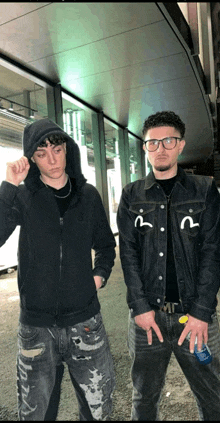 two young men standing next to each other with one wearing a hoodie and the other wearing glasses