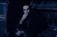 a man with long black hair is sitting in front of a sign that says " no smoking "