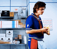 a man in a blue shirt is holding a banana in front of a shelf with boxes that say weekly