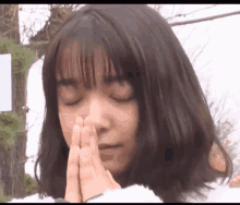 a young woman with her eyes closed is praying with her hands together .