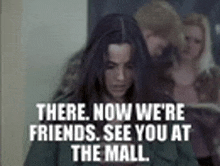 a woman is standing in front of a sign that says " there now we 're friends see you at the mall "