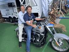 two men standing next to a harley davidson motorcycle in front of a trailer that says freedom rail