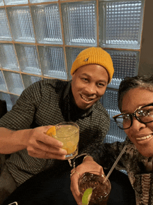 a man wearing a yellow beanie is toasting a woman with a drink