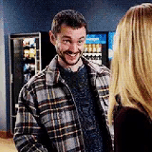 a man in a plaid shirt is smiling while talking to a woman in a room .