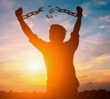 a silhouette of a man breaking chains at sunset