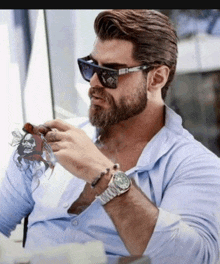 a man with a beard wearing sunglasses and a watch is smoking a cigar