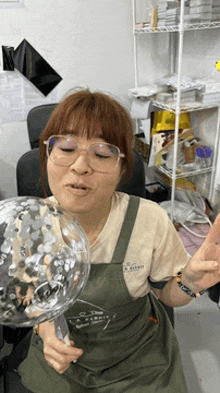 a woman wearing glasses is blowing up a clear balloon