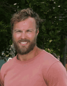 a man with a beard wearing a pink shirt is smiling