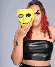 a woman with red hair is holding a yellow smiley face mask