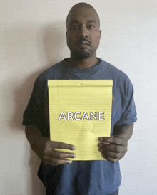 a man in a blue shirt is holding a yellow pad of paper with the word arcane on it