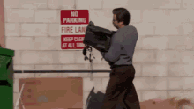 a man is carrying a bag in front of a sign that says no parking fire lane