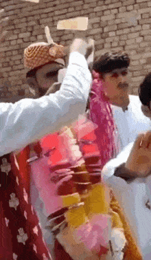 a group of people are standing in front of a brick wall and one of them is wearing a turban